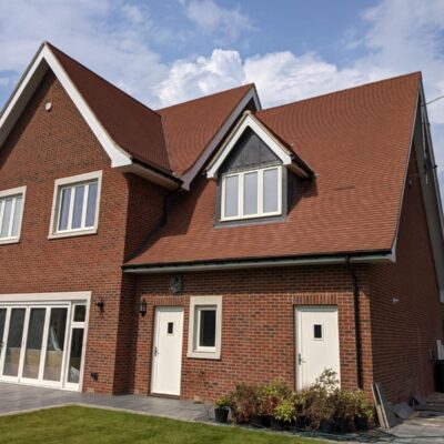 Modern Red Brick House with Gable Roof and White Doors on a Sunny Day